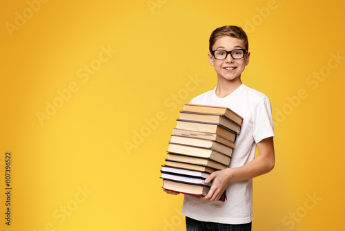 A young boy standing and holding a stack of books in his arms.