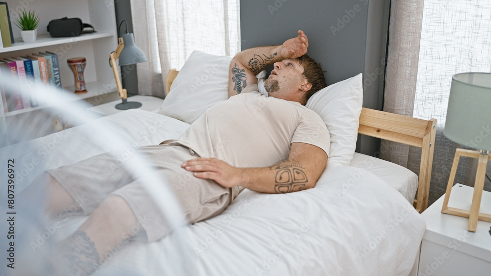 A young bearded man lounging in bed, with tattoos visible, inside a modern bedroom subtly hinting at relaxation and comfort. A young bearded man lounging in bed, with tattoos visible, inside a modern bedroom subtly hinting at relaxation and comfort.