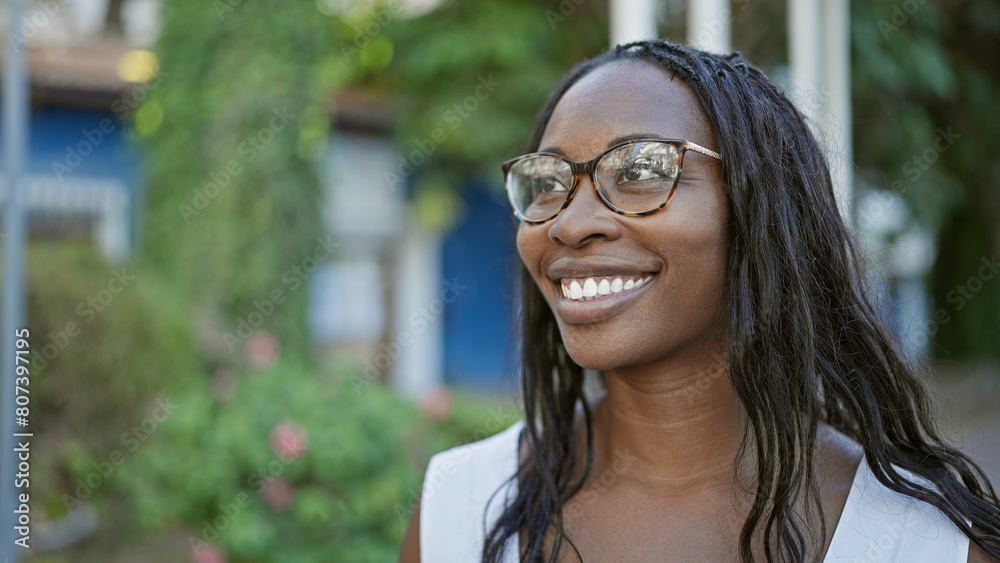 Portrait of a smiling young adult african american woman with curly hair wearing glasses outdoors in the city. Portrait of a smiling young adult african american woman with curly hair wearing glasses outdoors in the city.