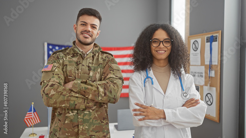 Quadro su tela A man in military uniform and a woman doctor standing with arms crossed in front of a usa flag, indoors