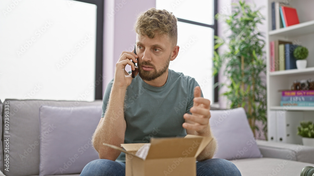 Caucasian man with blue eyes and beard talking on phone while unpacking a box in his cozy living room Caucasian man with blue eyes and beard talking on phone while unpacking a box in his cozy living room