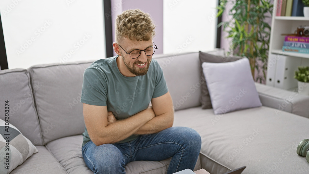 Caucasian young man with blue eyes and beard smiling while sitting on a sofa in a modern living room interior Caucasian young man with blue eyes and beard smiling while sitting on a sofa in a modern living room interior