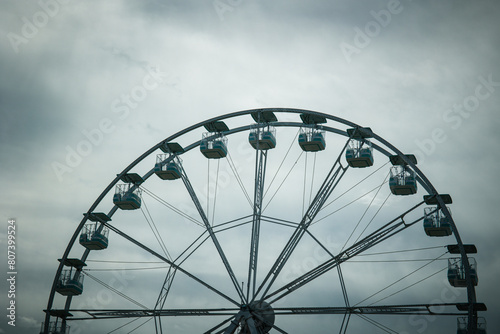 Wide angle views of a Ferris Wheel against a moody, cloudy sky. Vintage feeling, desolation. Nobody on the wheel. Industrial mood.