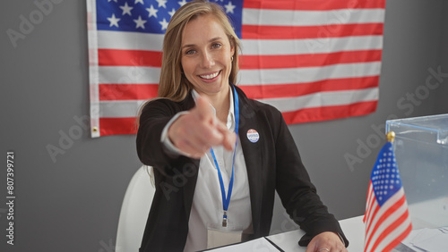Canvas Print Smiling woman points at camera in a voting center with american flag, showing civic participation