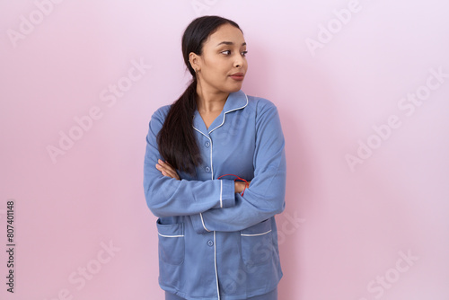 Young arab woman wearing blue pajama looking to the side with arms crossed convinced and confident