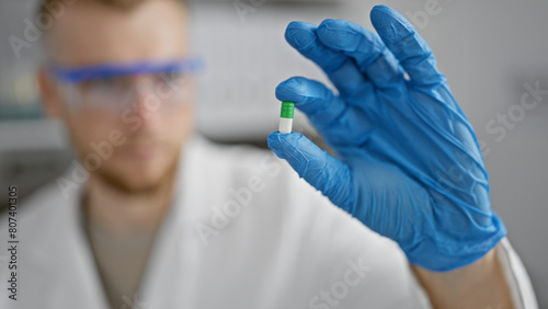 A young man in a lab coat examines a capsule with focus in a laboratory setting.