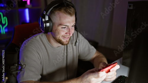 Handsome young caucasian man using smartphone in a dark gaming room at night photo