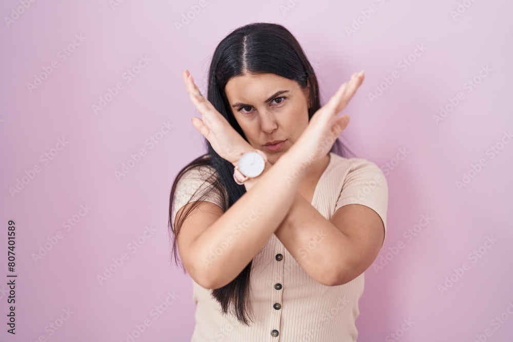 Young hispanic woman standing over pink background rejection expression crossing arms doing negative sign, angry face Young hispanic woman standing over pink background rejection expression crossing arms doing negative sign, angry face