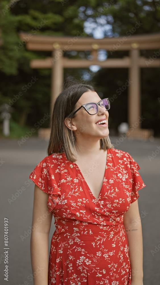Fototapeta premium Cheerful beautiful hispanic woman with glasses, happily standing, looking around, enjoying the positive vibes of tokyo's meiji temple