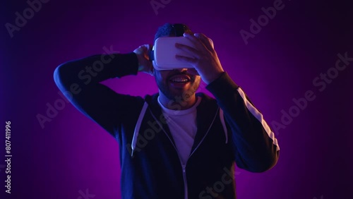 Imaginative and engrossed, the man reaches out into an unseen world as he plays an interactive virtual reality game, his face covered by the VR headset, surrounded by vibrant purple hues. Camera RAW.