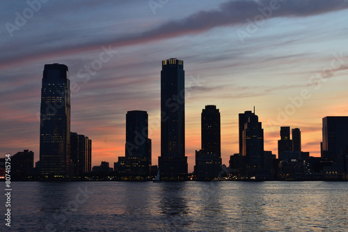 A city skyline with a beautiful sunset in the background. The buildings are tall and the water is calm