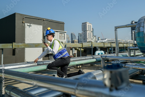 Wallpaper Mural An engineer attentively checks pipework on a rooftop against a cityscape, using a tablet for data analysis in urban maintenance. Torontodigital.ca