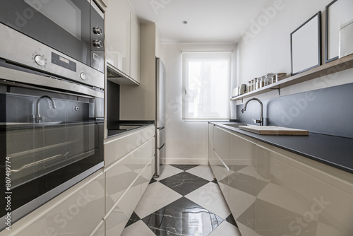 Modern kitchen furnished with black countertops and backsplashes and checkered floors and a window with a blind in the background photo