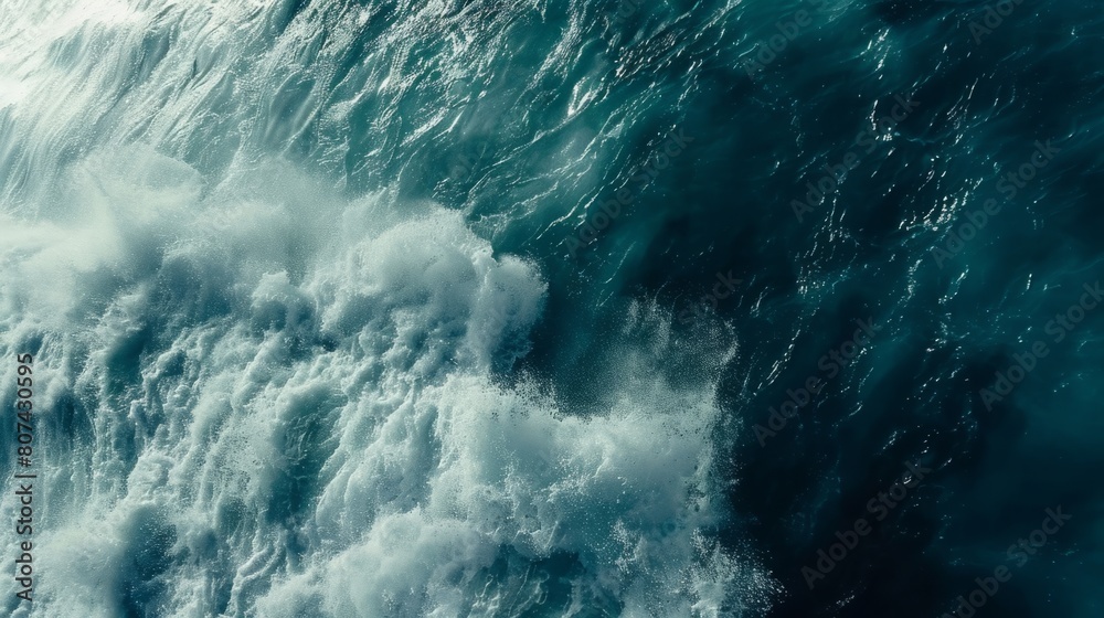 Fototapeta premium A birds eye view of the ocean waves crashing against the shore, creating foam and spray as they move towards the land.