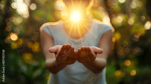 Woman holding open palms with a glowing light, empty space for book, crest. Concept symbolizing hope, healing, or spiritual energy in a serene natural setting with golden bokeh. © ArtStockVault
