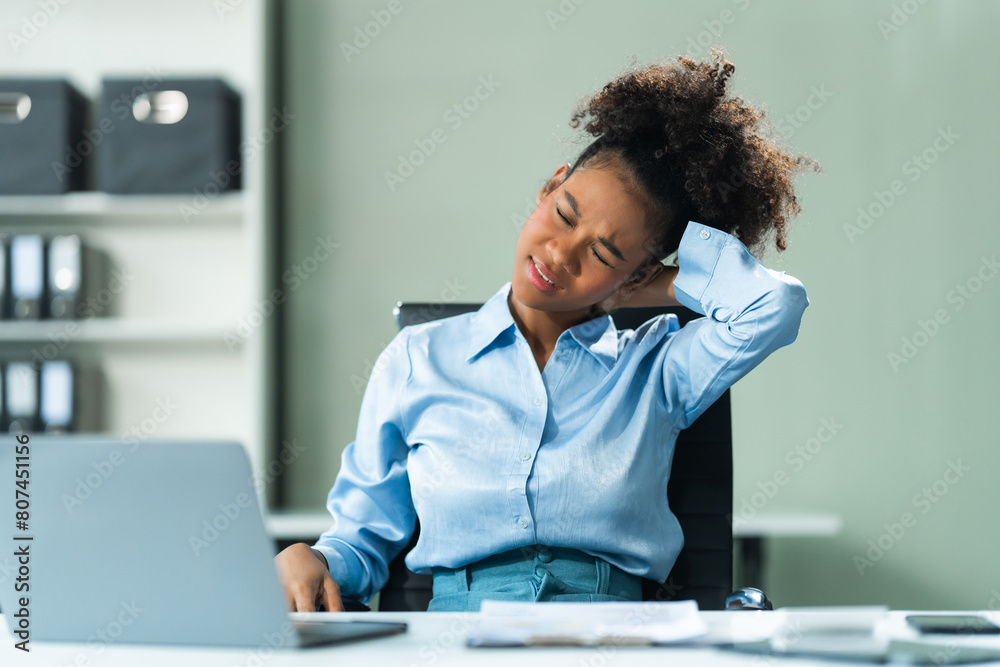 A young African American woman in a blue formal shirt with afro brown hair, suffering from office syndrome, navigates the challenges of being a businesswoman in a modern office. A young African American woman in a blue formal shirt with afro brown hair, suffering from office syndrome, navigates the challenges of being a businesswoman in a modern office.