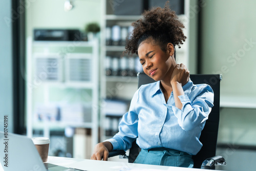 A young African American woman in a blue formal shirt with afro brown hair, suffering from office syndrome, navigates the challenges of being a businesswoman in a modern office. photo
