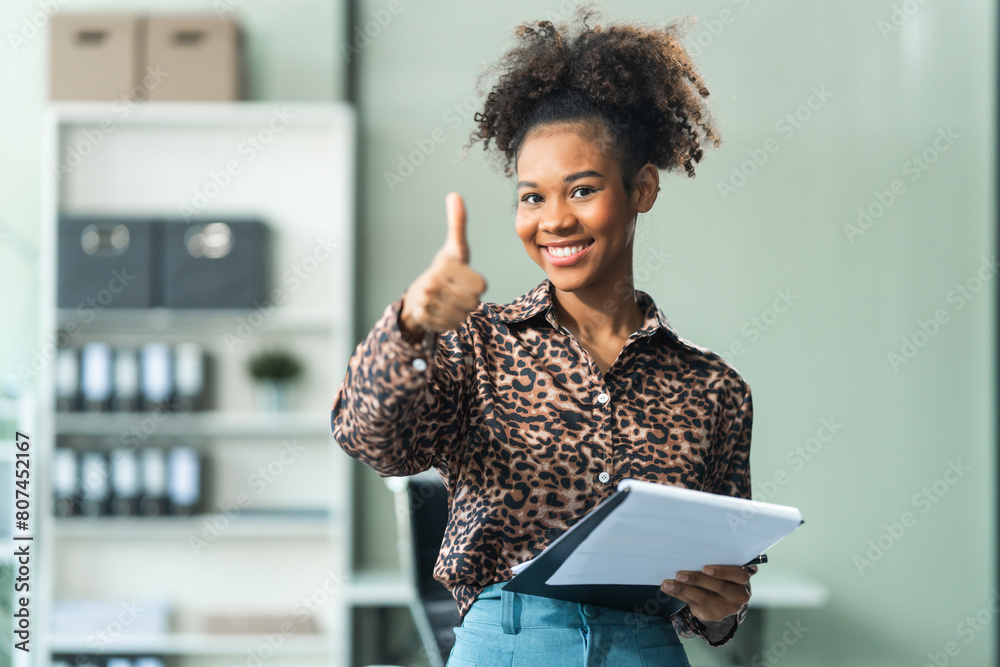 A young African American woman in a blue formal shirt with afro brown hair works as a product designer in a modern office, utilizing skills in design, CAD, CNC, and CNF. A young African American woman in a blue formal shirt with afro brown hair works as a product designer in a modern office, utilizing skills in design, CAD, CNC, and CNF.