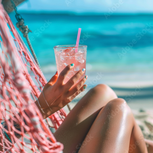 Hands with vivid nails clutching cold drink, pastel sea softly blurred. Summer relaxation with a cold drink and colorful nails on a hammock.
