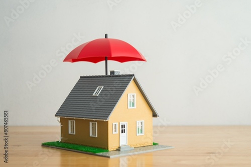 Red umbrella cover home model on wooden table with white background copy space. House, real estate, property insurance business, mortgage loan insurance concept. Insurance is risk control management.