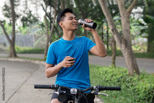 Asian Man Cycling in Blue Sports Shirt, Holding bottle or Drinking from Bottle concept. Healthy and sporty advertising concept photo