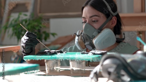Concentrated woman artist forming shapes from epoxy resin using stick. Serious craftswoman girl master in respirator thoughtfully, meditatively studies trains to work in liquid fluid art technique. photo