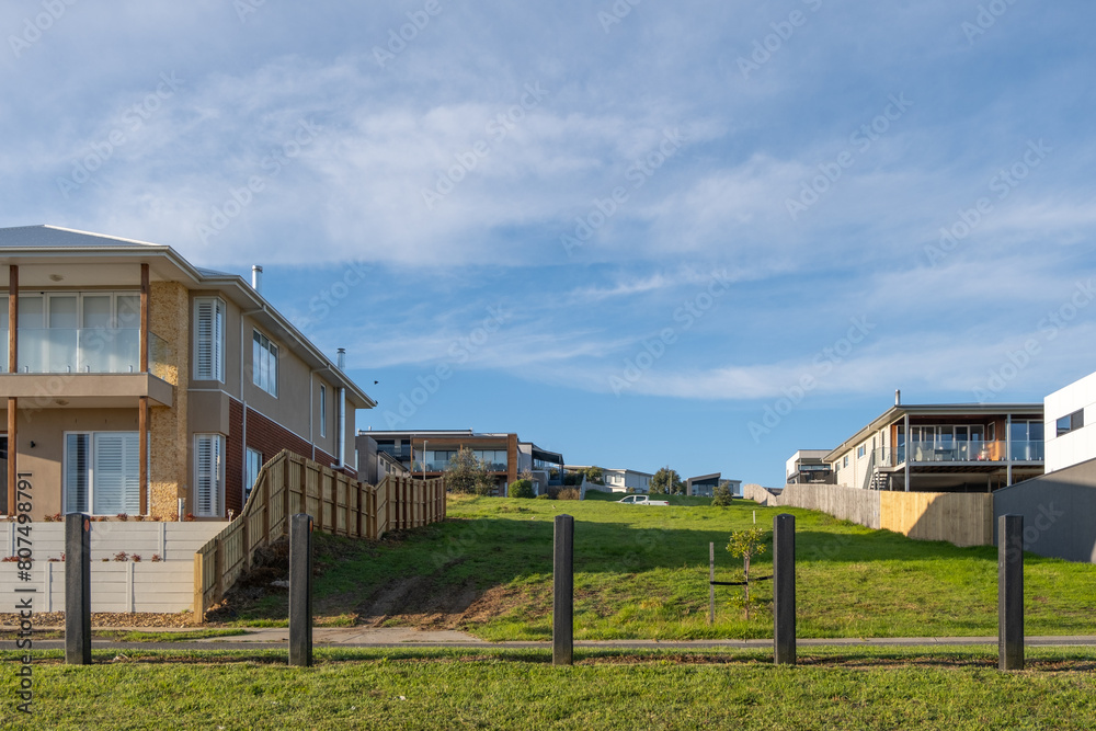 A vacant block of land surrounded by large and new suburban homes in a quiet residential neighbourhood. Concept of land for sale, real estate development, housing market, new developed estate. A vacant block of land surrounded by large and new suburban homes in a quiet residential neighbourhood. Concept of land for sale, real estate development, housing market, new developed estate.