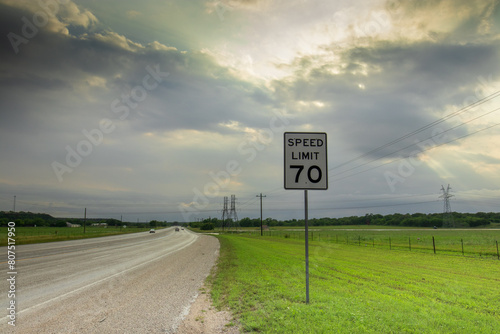 Fotografie On a tranquil Texas highway, a 70 speed limit sign demands notice, flanked by roadside grass and distant power lines vanishing into the horizon