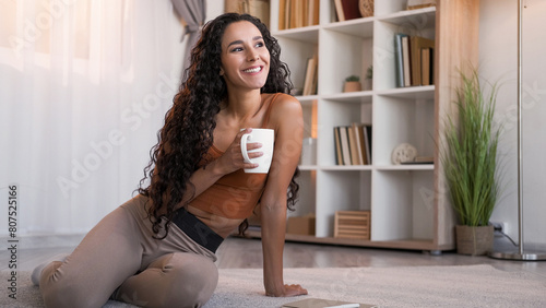 Morning coffee. Home leisure. Weekend rest. Happy relaxed smiling woman with mug daydreaming enjoying hot drink on floor at modern living room interior with free space. © golubovy
