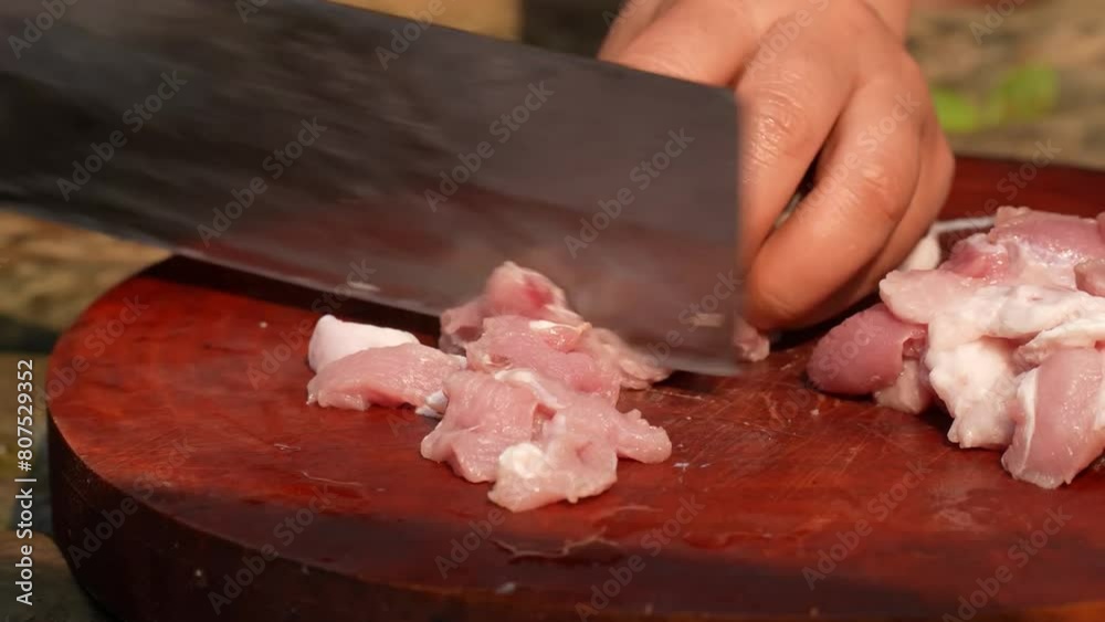 Hands chop and slice various cuts of raw meat on a wooden cutting board, using a sharp knife to prepare for cooking. Hands chop and slice various cuts of raw meat on a wooden cutting board, using a sharp knife to prepare for cooking.