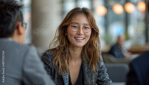 A photo of an Asian woman with long hair and glasses in business attire talking to someone out of focus in the background. Created with Ai