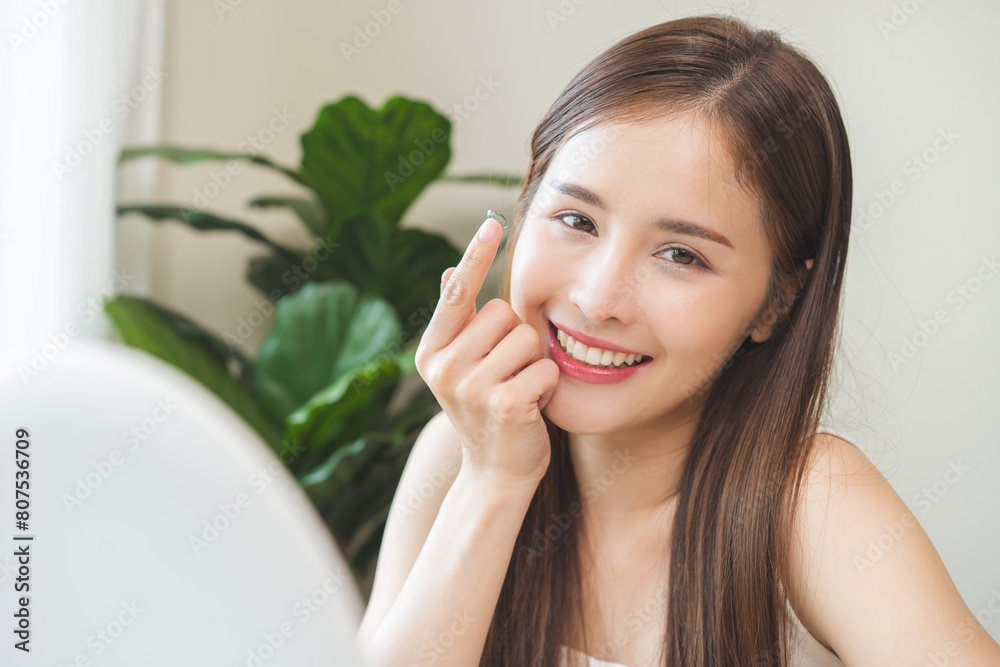 Ophthalmology care, eyesight or vision. Asian young woman, girl hand holding, wearing soft, daily disposable contact lens on her face with finger, looking in mirror at home. Medical and health care. Ophthalmology care, eyesight or vision. Asian young woman, girl hand holding, wearing soft, daily disposable contact lens on her face with finger, looking in mirror at home. Medical and health care.