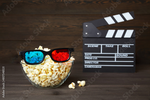Bowl of popcorn and 3D glasses for watching movies with friends in an online cinema on a dark wood background.