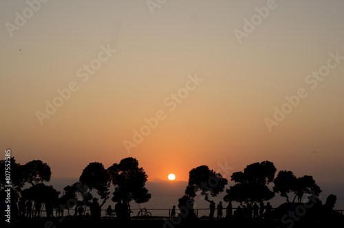 Wooden silhouette in orange sunset. People walking in the park in summer atmosphere.