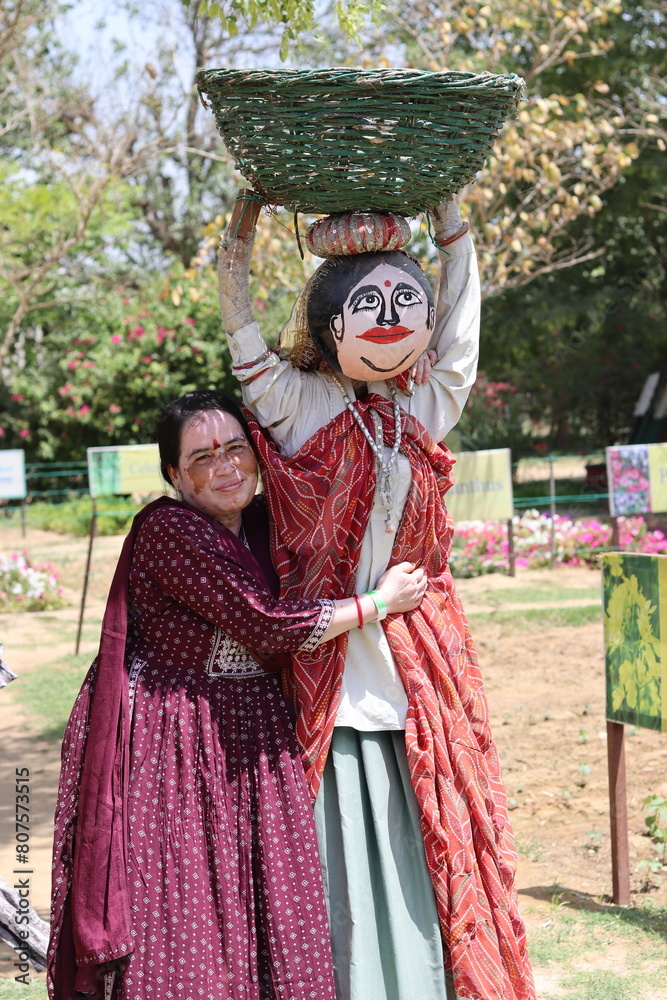 An Indian Lady hugging a Rajasthani Indian Scarecrow holding a basket in bright sunlight
