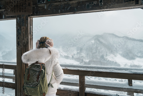 Woman tourist sightseeing view of village with snow in winter from mountain viewpoint of Yamadera temple or Risshakuji temple located in Yamagata City, in Yamagata Prefecture, Tohuku, Japan photo