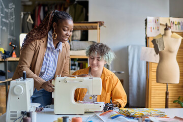 Portrait of smiling teen girl with disability using sewing machine in vocational training class with social worker helping copy space