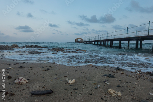 waves with foam at the beach with a long jetty at the sea