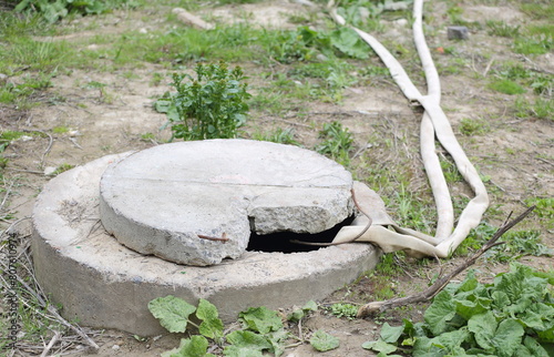 Two canvas hoses are lowered into a concrete manhole with a broken lid
