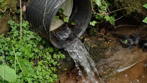 Industrial polluted waste water flowing from a black sewer pipe into a river in close up in slow motion. Global warming concept