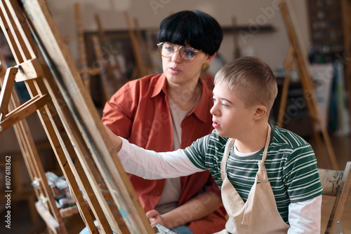 Side view portrait of young boy with Down syndrome painting on easel in art class enjoying creative activity © Mediaphotos