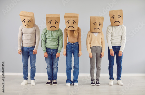 Tableau sur toile Diverse people group wears paper bags on their heads, each adorned with a drawn sad face