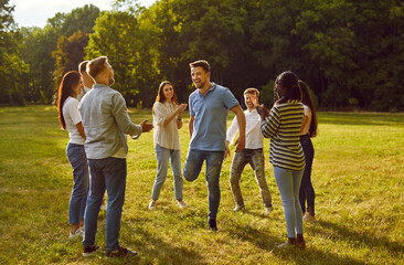 Portrait of a group of excited happy young people friends or colleagues having fun hanging together in nature in the park. Happy students playing games outdoor on a sunny summer day.