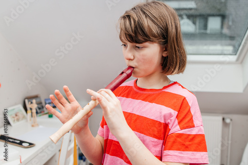 A teenage girl learns to play the flute and rehearses at home. Music school, music as a hobby for teenagers