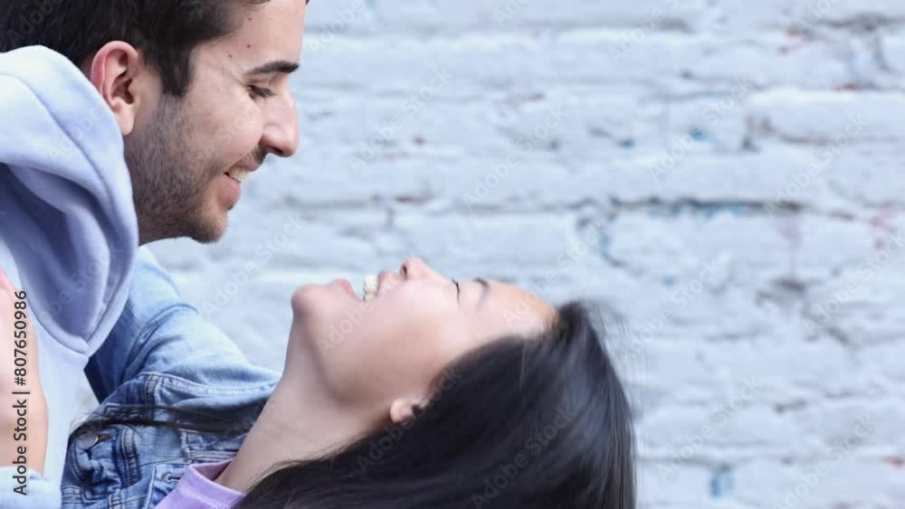 Young man and asian woman kissing by a blue brick wall.  Young interracial couple enjoying their date in the city.