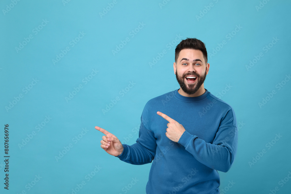 Happy young man with mustache pointing at something on light blue background. Space for text Happy young man with mustache pointing at something on light blue background. Space for text