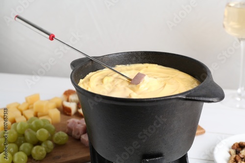 Dipping ham into fondue pot with tasty melted cheese at table  closeup