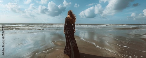 rear view of woman in long black dress standing alone on beach