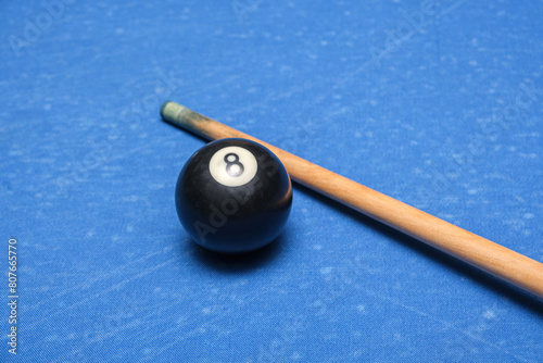 Close-up of an eight ball on pool table. Black 8-ball and cue tip on blue billiard table.