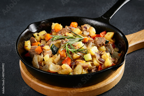 Savory cast-iron skillet ragout with tender meat and colorful vegetables on a textured black table